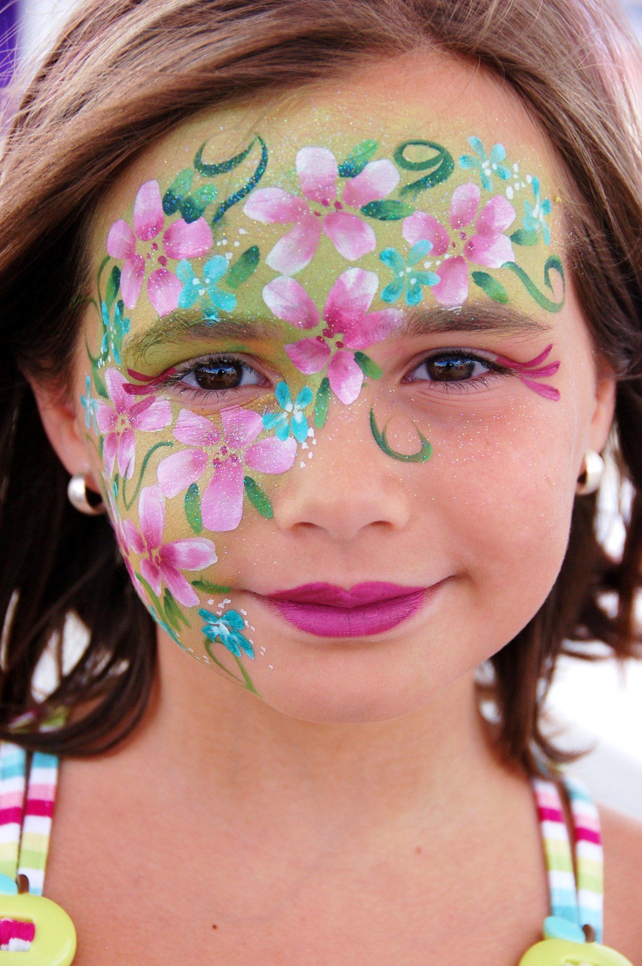 Beautiful floral face paint design with pink cherry blossoms and turquoise accents.