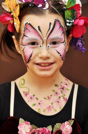Pink butterfly face paint design with floral crown and neck decoration.
