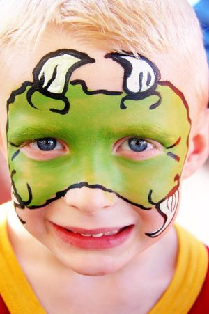 Green mask face paint design with white bone details resembling a dinosaur.