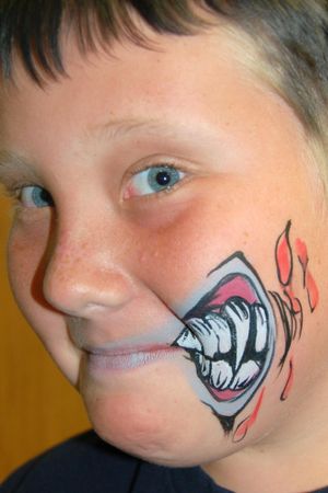 Creative face painting shows a cartoon-style monster mouth with sharp teeth on one cheek.