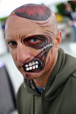 Dark and dramatic monster face paint design covers half of face with exposed teeth and sinister eye.