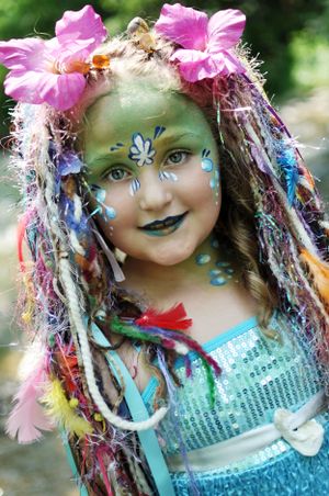Colorful fantasy costume with teal face paint, pink flowers, and glittery decorative hair accessories at a Renaissance festival.