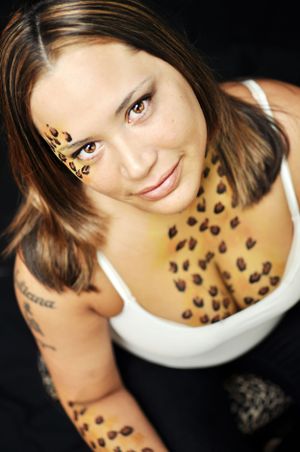 Creative portrait shot against black background showing leopard print body art design and white tank top.