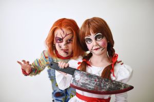 Two people wearing Halloween costumes and face paint depicting horror characters pose together, Chucky and Annabelle.