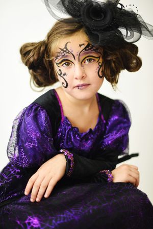 Elegant gothic makeup with black swirls and purple dress paired with a black fascinator.