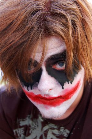 Dark dramatic face paint design featuring black eye makeup and red lipstick in joker style.