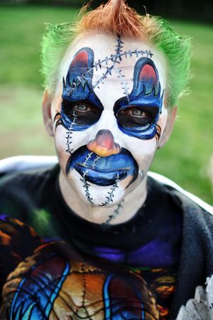 Blue and white clown face paint design with stitched details and dark eye makeup.