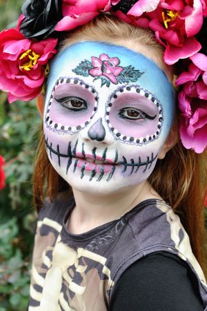Sugar skull face painting with pink flowers and dotted details in Day of the Dead style.