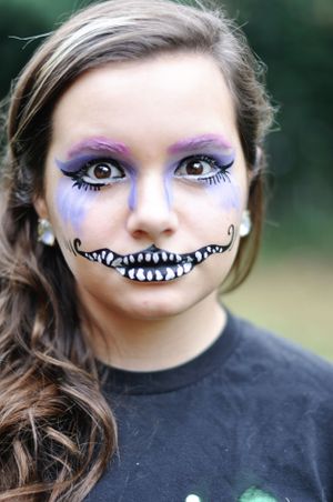 Creative Halloween makeup featuring purple eyeshadow and drawn-on teeth in cheshire cat style.