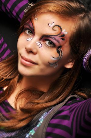 Fantasy face paint design with purple swirls and sparkles on dark background.