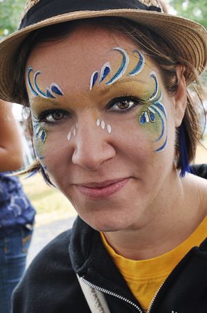 Peacock-inspired face paint design with blue and green swirls worn with a brown hat.
