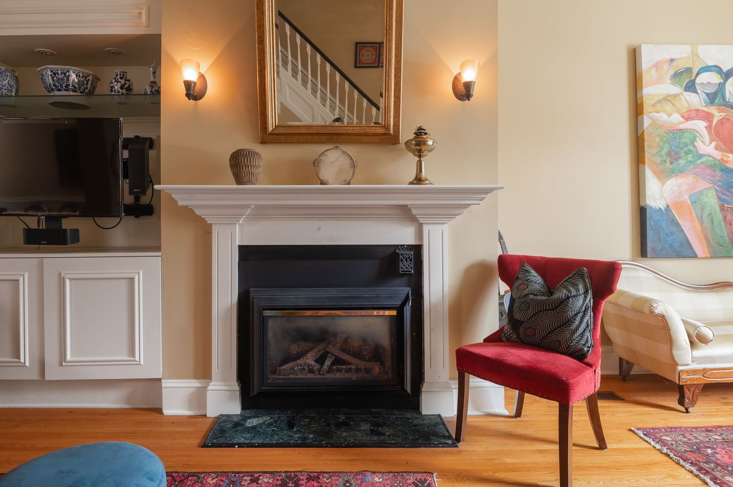 A cozy living room interior with white fireplace mantel, red accent chair, and decorative wall art above the hearth.