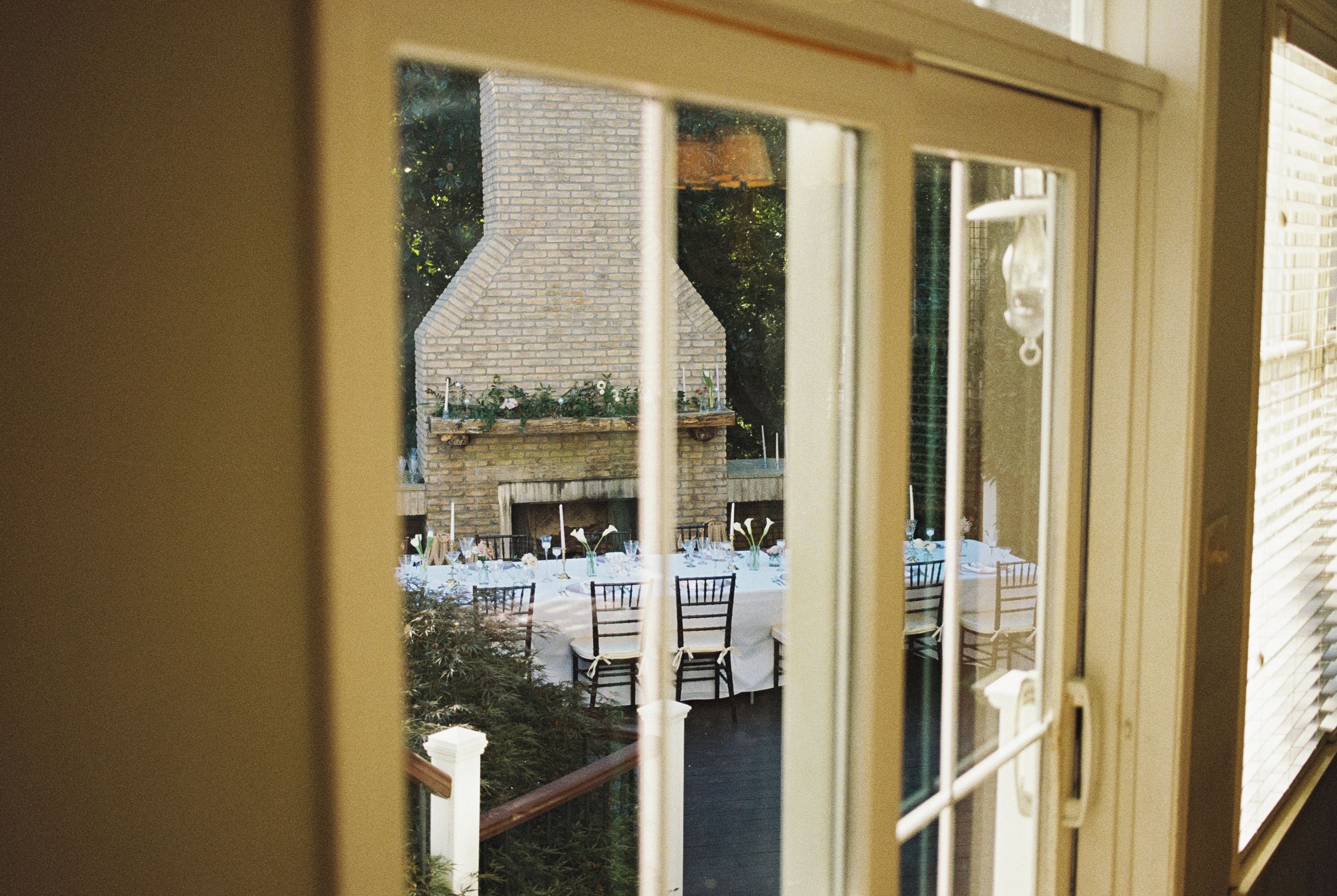 View through glass doors of an elegant wedding reception setup with white chairs and tables in a sunlit venue.