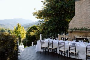 An elegant outdoor wedding reception setup with dark chairs and white tablecloths overlooking mountain views.
