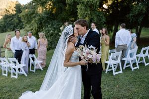 Romantic garden wedding ceremony with white chairs and lush greenery backdrop as newlyweds share an intimate moment.