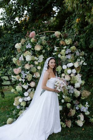 An elegant floral arch made of white and pink hydrangeas creates a romantic wedding backdrop in a garden.