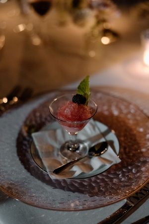 A pink sorbet dessert garnished with mint and berries served in a martini glass on an ornate plate.