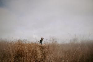 A silhouette of two people embracing in tall grass against a cloudy sky.
