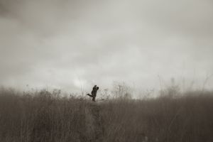 Two silhouettes walk together against a moody cloudy sky on a hilltop.