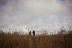 Dark figures stand together on a hill surrounded by dry winter grass.