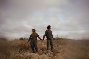 Couple holding hands while walking through a golden field at dusk.