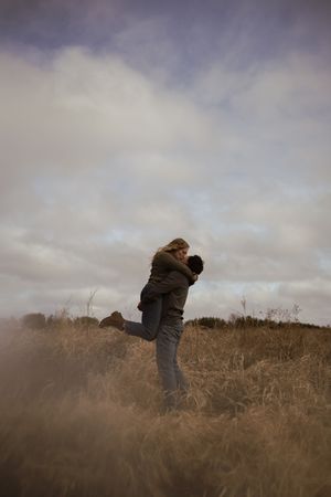Two people embrace while standing in a field under overcast skies.