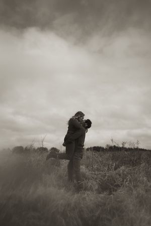 Figures embrace in a misty field during an overcast day.