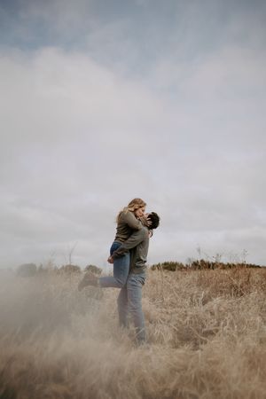 A romantic embrace in a field of golden grass under an overcast sky.