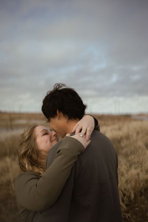 Two people share a close romantic moment against a moody sky and golden field landscape.