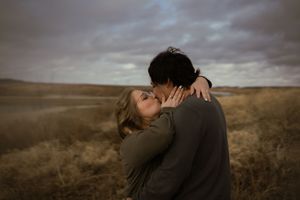 Intimate embrace captured against dramatic cloudy landscape.