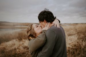 Intimate couple moment captured in a golden field with overcast sky.
