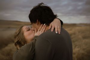 A couple embraces tenderly in a field during an overcast day, creating an intimate and romantic moment.