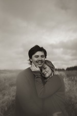 Two people share joyful laughter while embracing in a field under moody skies.