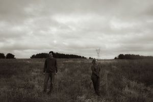 People exploring a vast autumn field beneath dramatic cloudy skies at dusk.