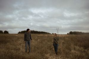 Silhouettes of people walking through a rustic prairie landscape with stormy clouds overhead.