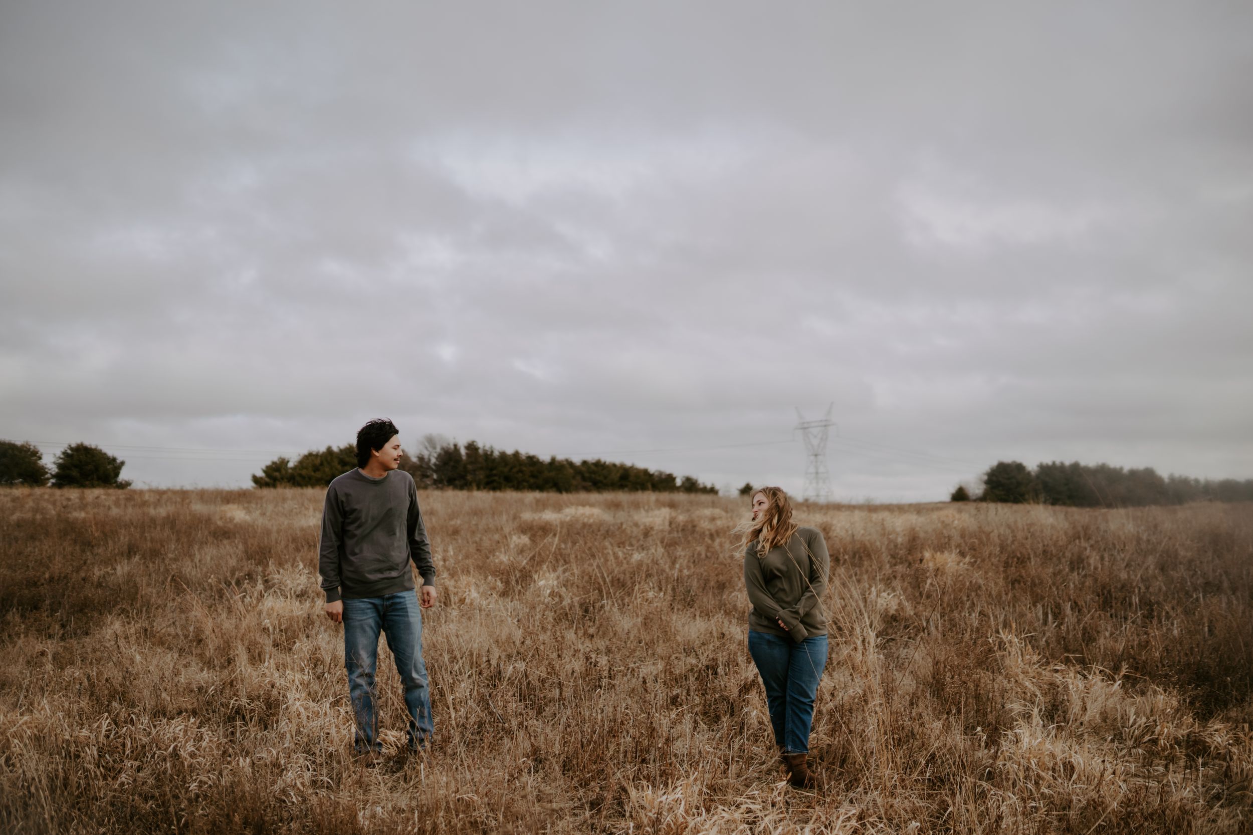 A couple walking together through a golden field under cloudy skies.