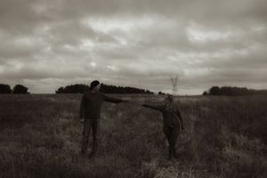 Two people wandering through tall grass in a rural field during an overcast evening.