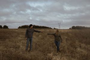 People exploring a windswept prairie field under moody gray skies.
