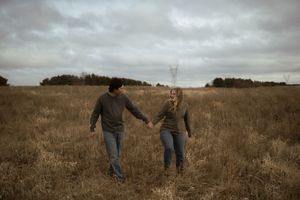 A couple walking hand in hand through a rustic prairie field.