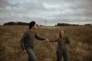 A couple shares a playful moment in a golden field during sunset.