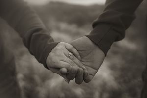 Close-up of hands clasped together against a soft, blurred natural background.