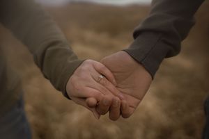 Two hands tenderly clasped together against a moody cloudy sky and natural landscape background.