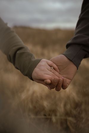 Close-up of intertwined hands with a ring visible against a blurred outdoor background.