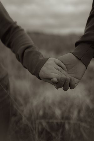 Intimate black and white photo of two hands holding each other in a grassy field.