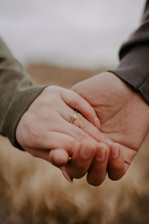 Close-up of hands with engagement ring against blurred natural background.