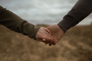 Artistic shot of hands reaching out to hold each other against a dramatic sky.