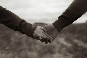 Sepia-toned photograph of hands gently clasped together with tall grass in the background.