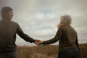 Two people in warm clothing holding hands while walking through an autumn field.