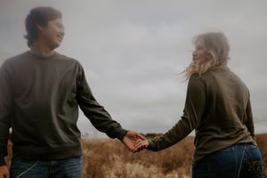 Couple walking hand in hand through tall grass in an autumn field.