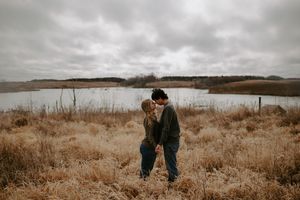 Wide landscape shot of a couple walking through golden fields near water.